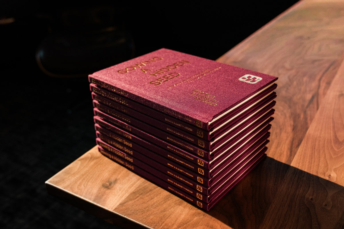 A large stack of Sowing a Hidden Seed marriage devotionals on a wooden table